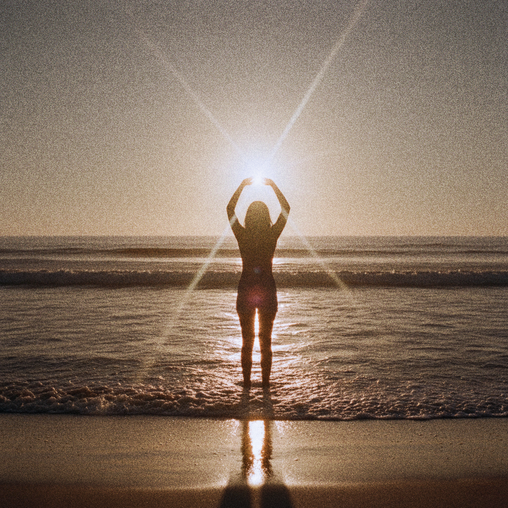 Silhouette of a person standing by the ocean at sunset, holding their hands around the sun as its light creates a starburst effect.